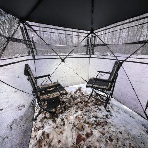 2-_2_720x - North American Bow Hunter Two folding camping chairs facing each other inside a clear, snow-covered tent with leaf litter on the ground outside.",
