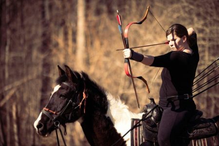 Picture1 - North American Bow Hunter Woman archer riding a horse, drawing a bow in a forest setting.